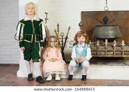 Two boys and girl in medieval costumes pose near fireplace with boiler.