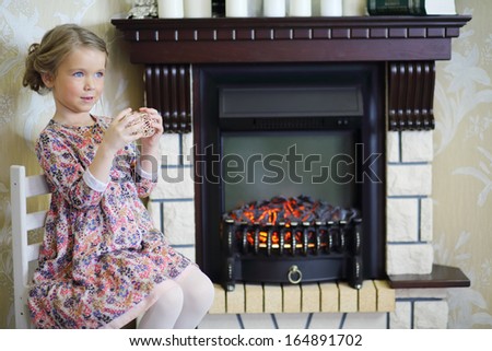 Little cute girl with straw balls sits on chair near fireplace in cosy room and looks away.