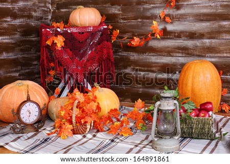 Orange big pumpkins, old lamp, clock and basket of fruits on rug in room with autumn interior.