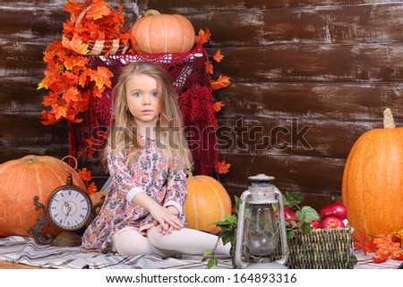 Pretty little girl in dress sits on floor in room with pumpkins and autumn interior.