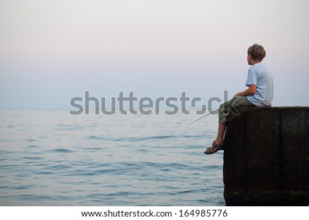 A young boy with a fishing rod sitting on the rock and fishing in the sea
