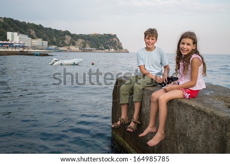A young brother and sister fishing in the sea with a fishing rod