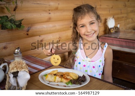 Little smiling girl sitting in a cafe at the table with food