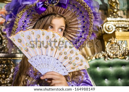 The girl in old-fashioned dress and hat hid her face behind a fan, focus on a fan.