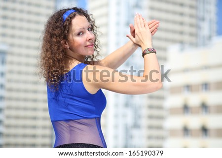 Woman in a blue suit and a scarf on hips looks back at the back and clapping against the background of a multistory residential complex