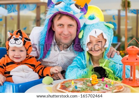 Father with daughter in monster costumes and baby boy in tiger costume celebrate the birthday in a cafe