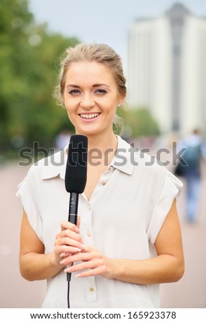 Girl reporter in white blouse and with a microphone on the street
