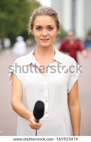 Professional reporter young girl holds out a microphone on the street