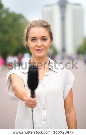 Professional reporter beautiful girl standing on the street and holds out a microphone