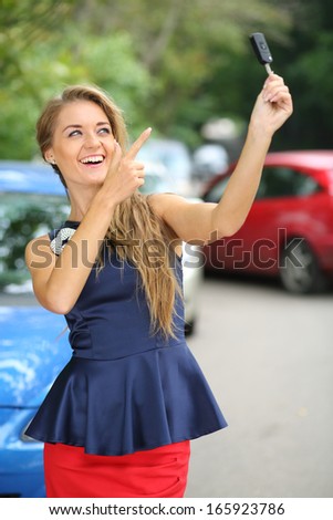 Happy beautiful girl holding car key and points a finger at it