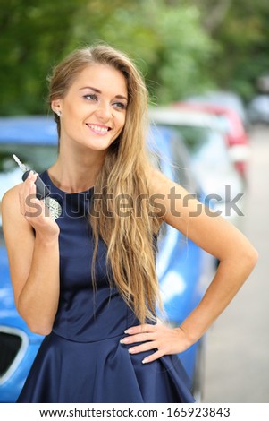 Smiling beautiful girl standing on the street and holding car key in hand