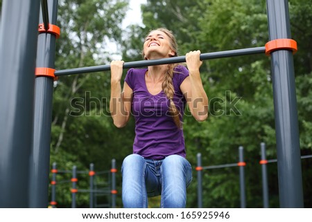 Young beautiful girl doing chin-ups on the outdoor sports ground