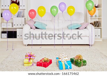 Room with big sofa, gift boxes on the floor and birthday air balloons hanging in the air