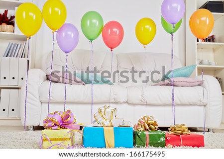 Light room with carpet on the floor and big sofa, gift boxes are on the carpet and birthday air balloons hang in the air