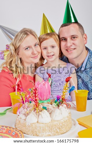Mother, father and little daughter sit cheek to cheek at birthday table
