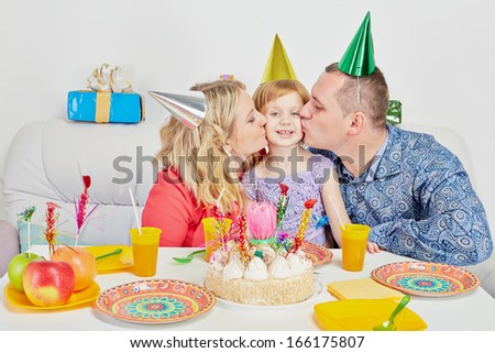 Mother and father kiss their daughter when they sit at birthday table