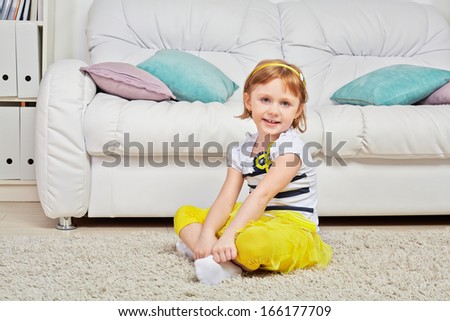 Smiling little girl sits on light carpet in room near to big sofa