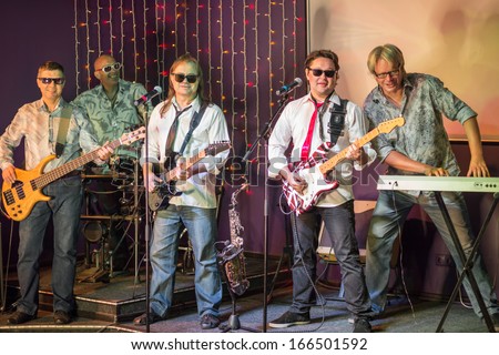 The musical group of five men with with musical instruments performs on stage in a club