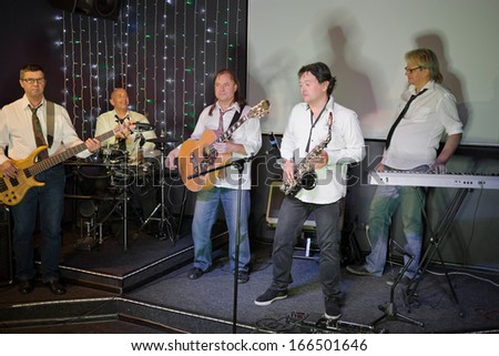 The musical group of five men in white shirts and ties performs on stage in a club