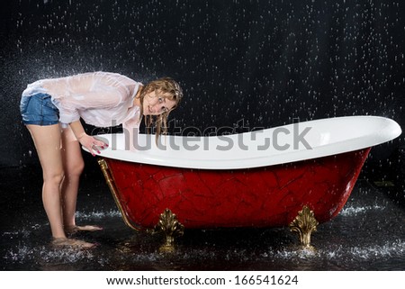 Wet girl bent over the bathtub under the spray of water