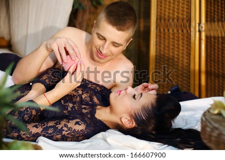 Beautiful woman and man lie on bamboo bed and man gives peach to woman in bedroom. Focus on woman.