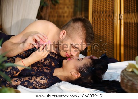 Beautiful woman and man lie on bamboo bed and touch each other noses in bedroom.