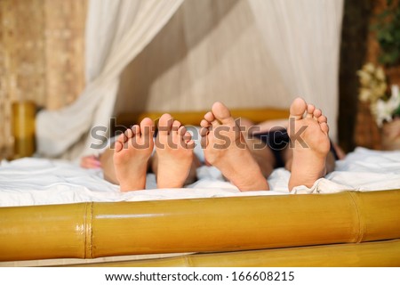 Male and female feets on bamboo bed with white linen in bedroom.