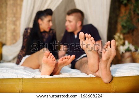 Feets of talking man and woman on bamboo bed with white linen in bedroom.