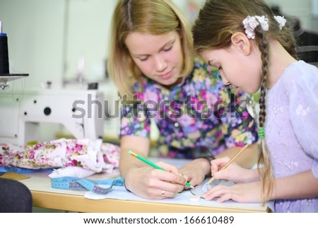 Female tailor teaches student girl use of templates near sewing machine. Focus on girl.