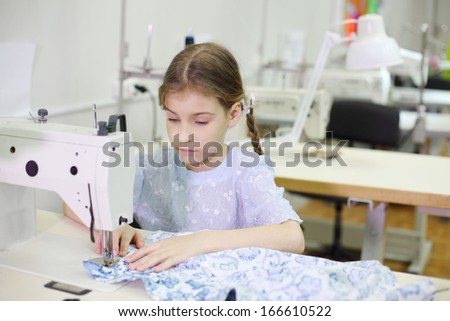 Student girl sews at white sewing machine in classroom with many machines.