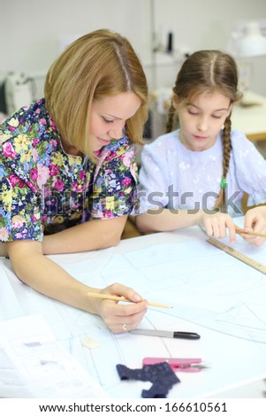 Smiling female tailor and student girl draw patterns for clothes. Focus on woman.