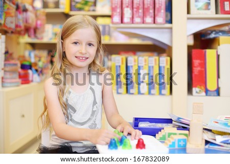 Little pretty girl with long blonde hair plays with toys in store.