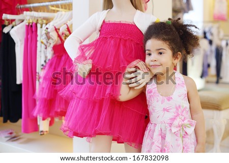 Little pretty girl holds hand of dummy and looks away in children store.