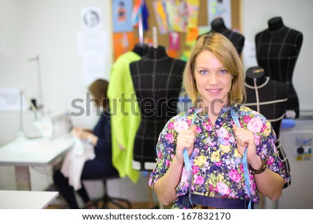 Happy female tailor holds blue tape and stands near four black mannequins.