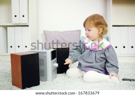 Little cute girl looks at music system on carpet in room at home. Shallow depth of field.