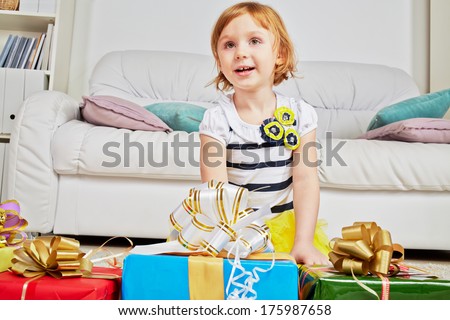 Portrait of little girl sitting on knees on carpet with gift boxes