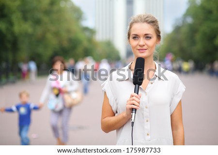Young reporter standing in the street with a microphone in her hand and looking away