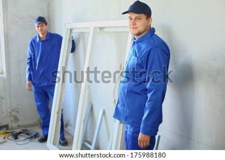 Two men in work clothes with the new window frame in a room under renovation