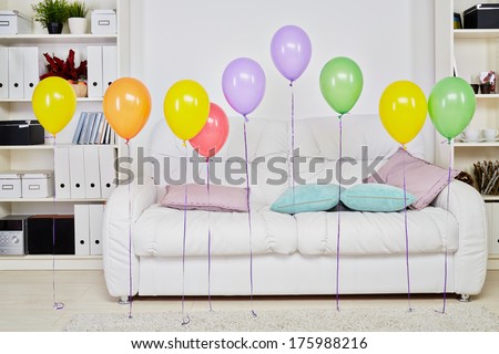 Interior of room with big soft white sofa, light carpet on  floor and row balloons hanging in air