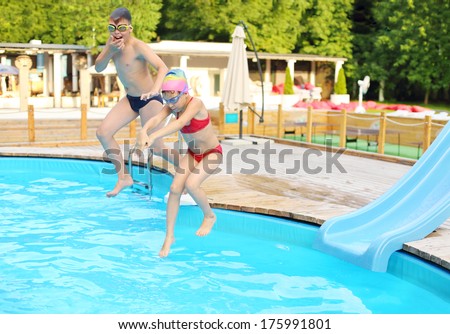 Happy boy and girl jumping into the outdoor swimming pool at summer day