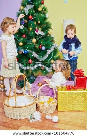 Three children decorate christmas tree, girl hangs blue star, another one holds golden ball