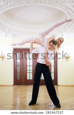 Young dancer holds ballerina in sexy costume on shoulder near door in room