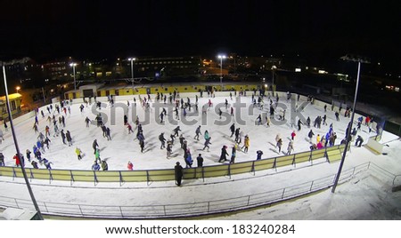 People skate on big ice rink at dark winter night. Aerial view