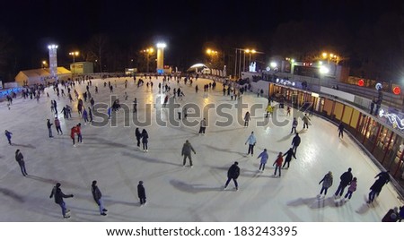 Many people skate on big rink in winter night. Aerial view