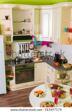 Little girl upside down holds a shelves in the kitchen with table and dishes