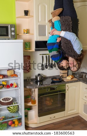 Mother with son stand upside down in the kitchen with open fridge