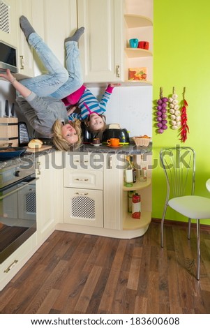 Mother and daughter sitting at shelves upside down in the colored kitchen