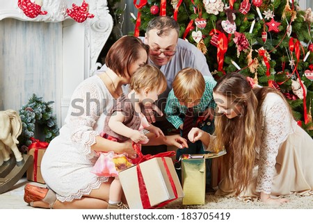 Family of five all together looks into gift box, sitting under Christmas tree