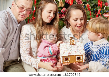 Family of five gathered under Christmas tree around gingerbread in hands of mother