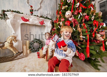 Little boy and little girl sit on big gift boxes under Christmas tree, holding open gift boxes of smaller size